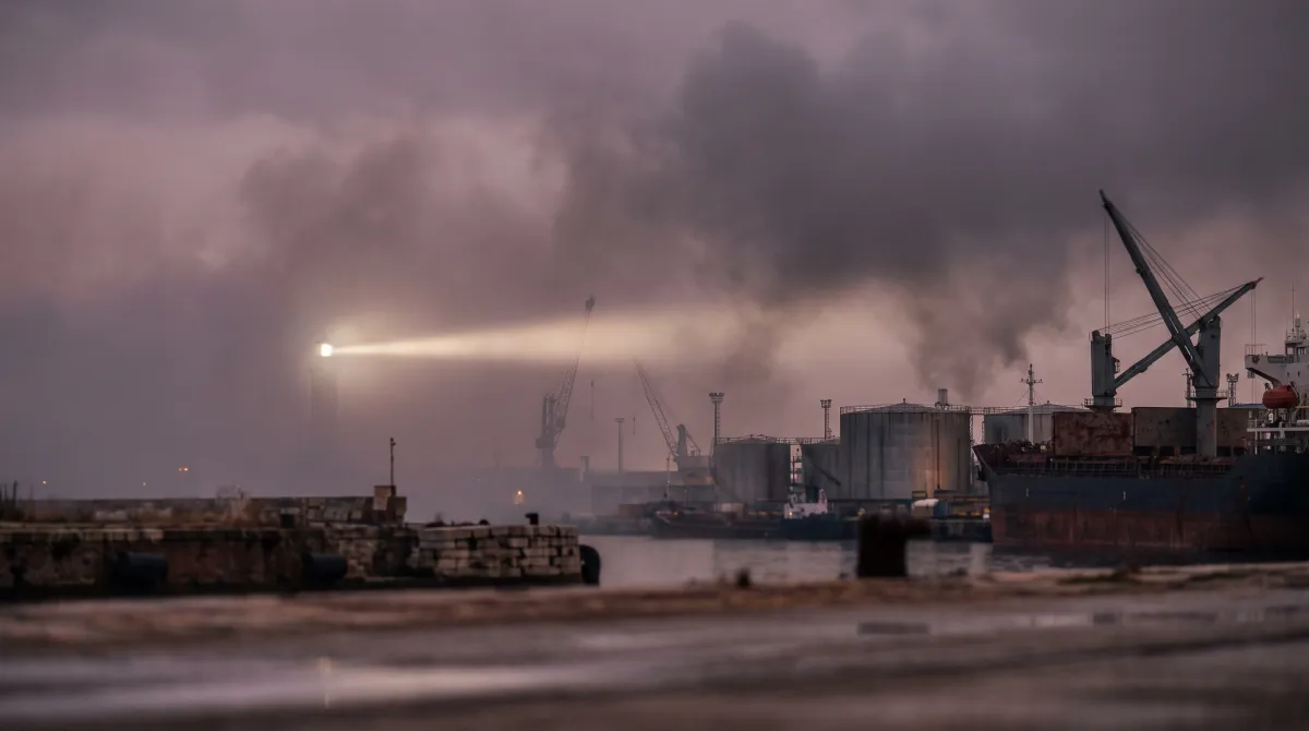 Fascio di un faro nella nebbia serale sopra un porto industriale